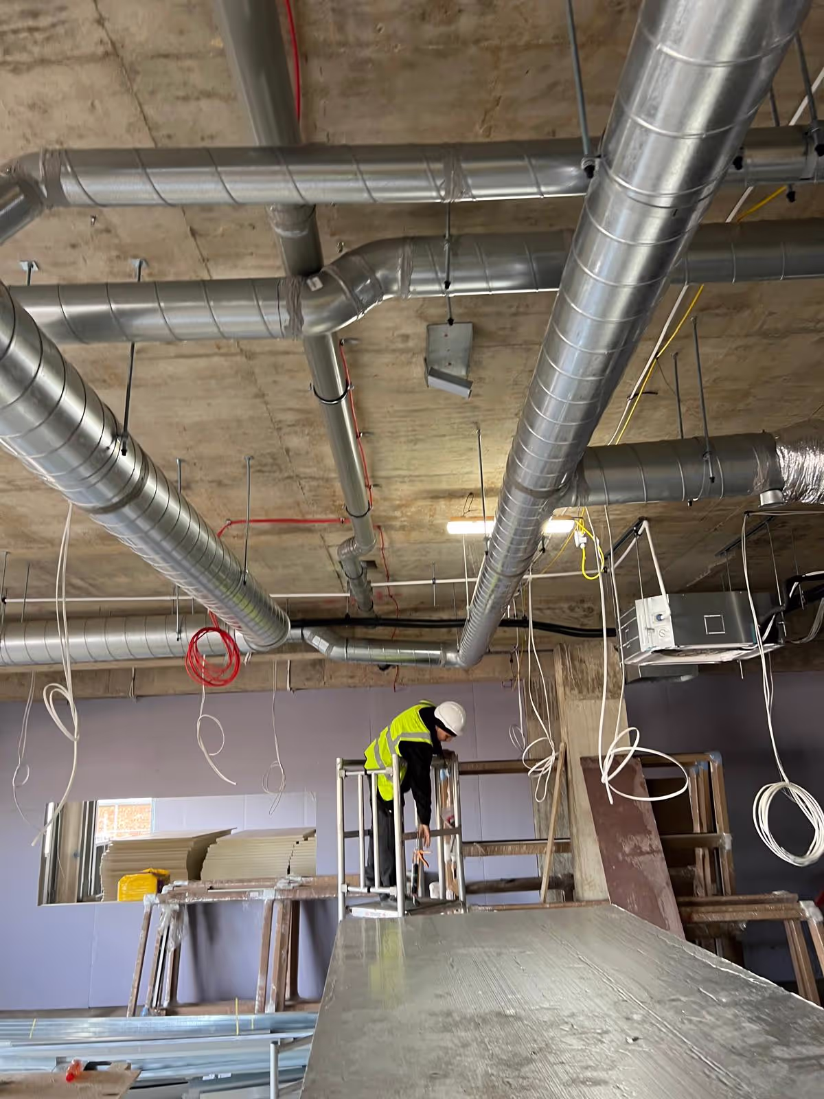Commercial metal ductwork being installed along a concrete ceiling