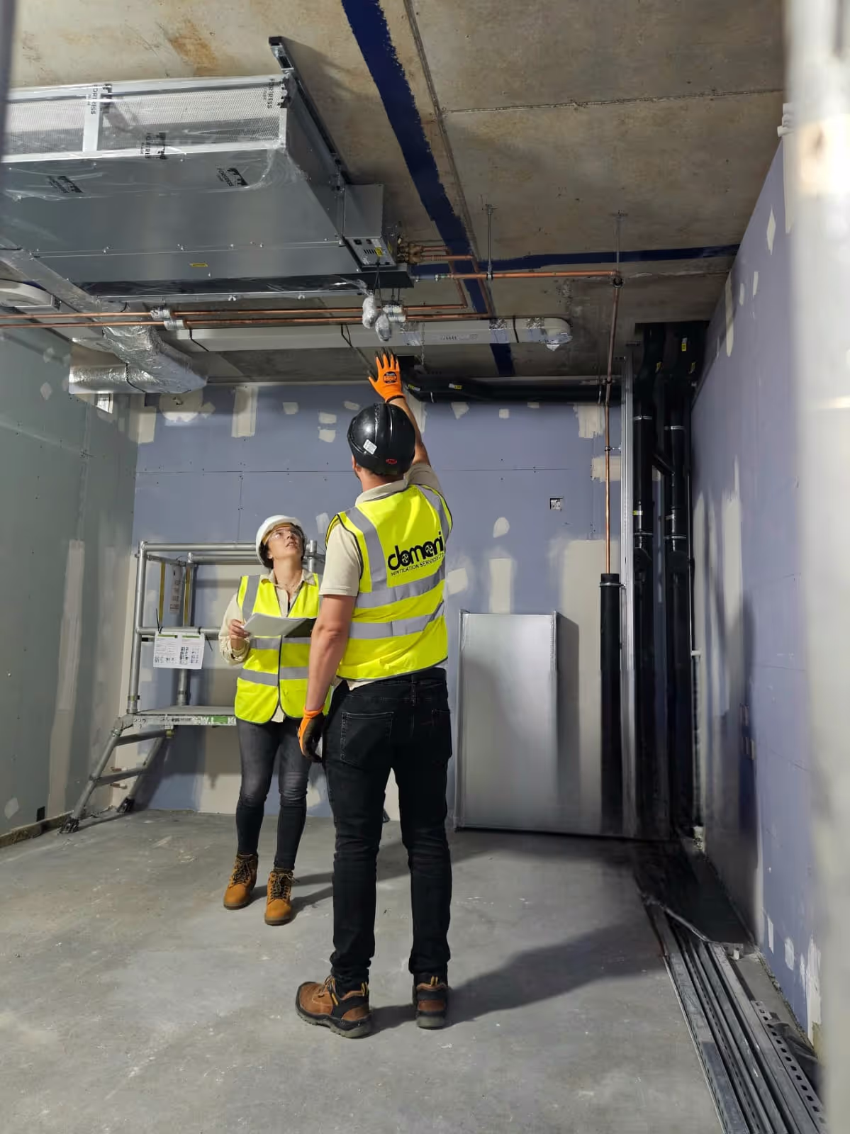 Two engineers inspecting a ceiling-mounted ventilation unit on site