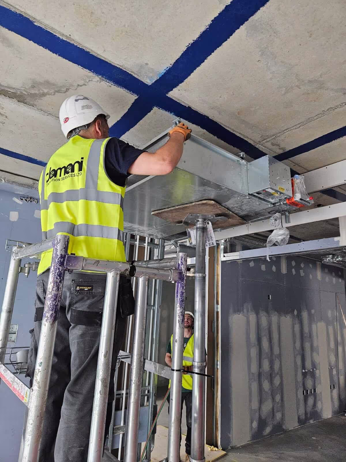 NICEIC-certified Domani Ventilation technician commissioning an MVHR unit from a ladder